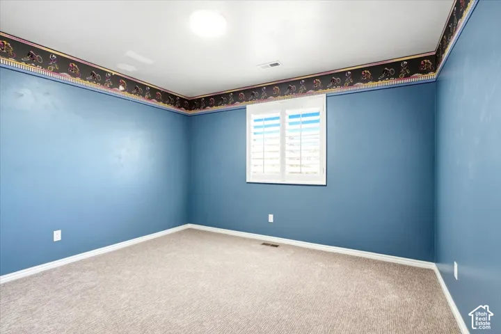Carpeted room with a ceiling-mounted light fixture and a window with plantation shutters