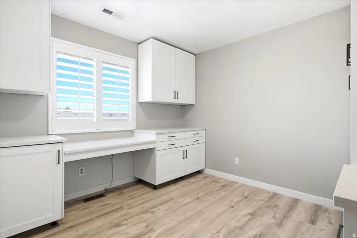 Built-in desk area with white cabinetry, light-toned countertops, and wood-finish flooring