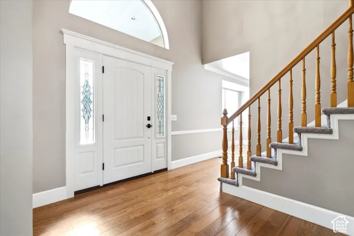 Hardwood-finish flooring, a grand entry door with decorative glass sidelights, an arched transom window, a two-story foyer, and a staircase with wood newel posts and spindles