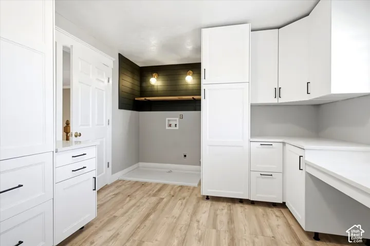 Integrated laundry area featuring wood-finish flooring, white cabinetry, dark accent wall paneling, and a built-in shelf