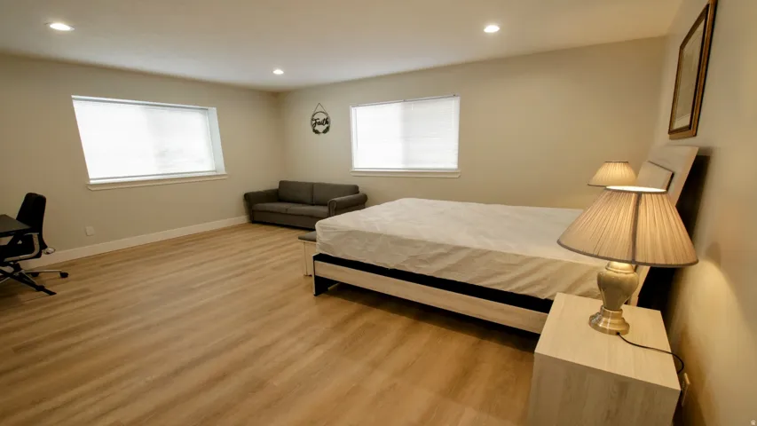Recessed lighting, light wood-finish flooring, two windows with blinds, neutral wall paint, and a built-in upholstered headboard