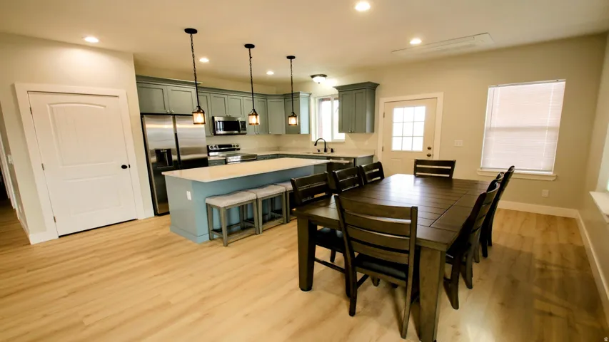 Open-concept living space featuring wood-finish flooring, recessed lighting, and a kitchen with stainless steel appliances, pendant lighting, and light-toned cabinetry