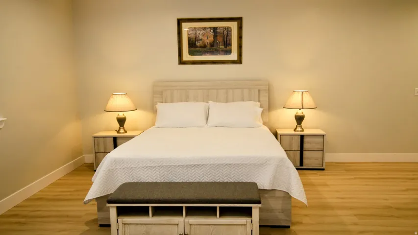 Wood-finish flooring with light-toned walls, featuring a slat-style headboard and a built-in storage bench