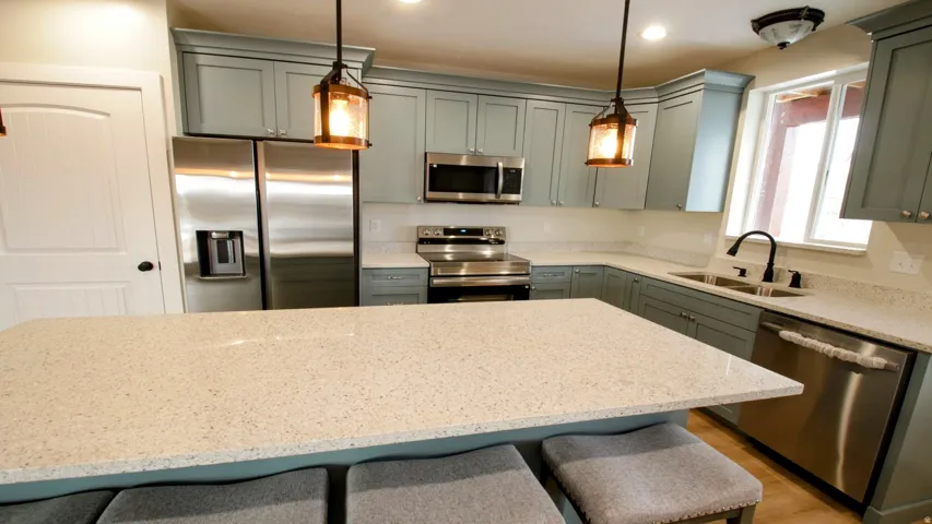 Kitchen featuring light blue cabinetry, stainless steel appliances, speckled white countertops, and pendant lighting