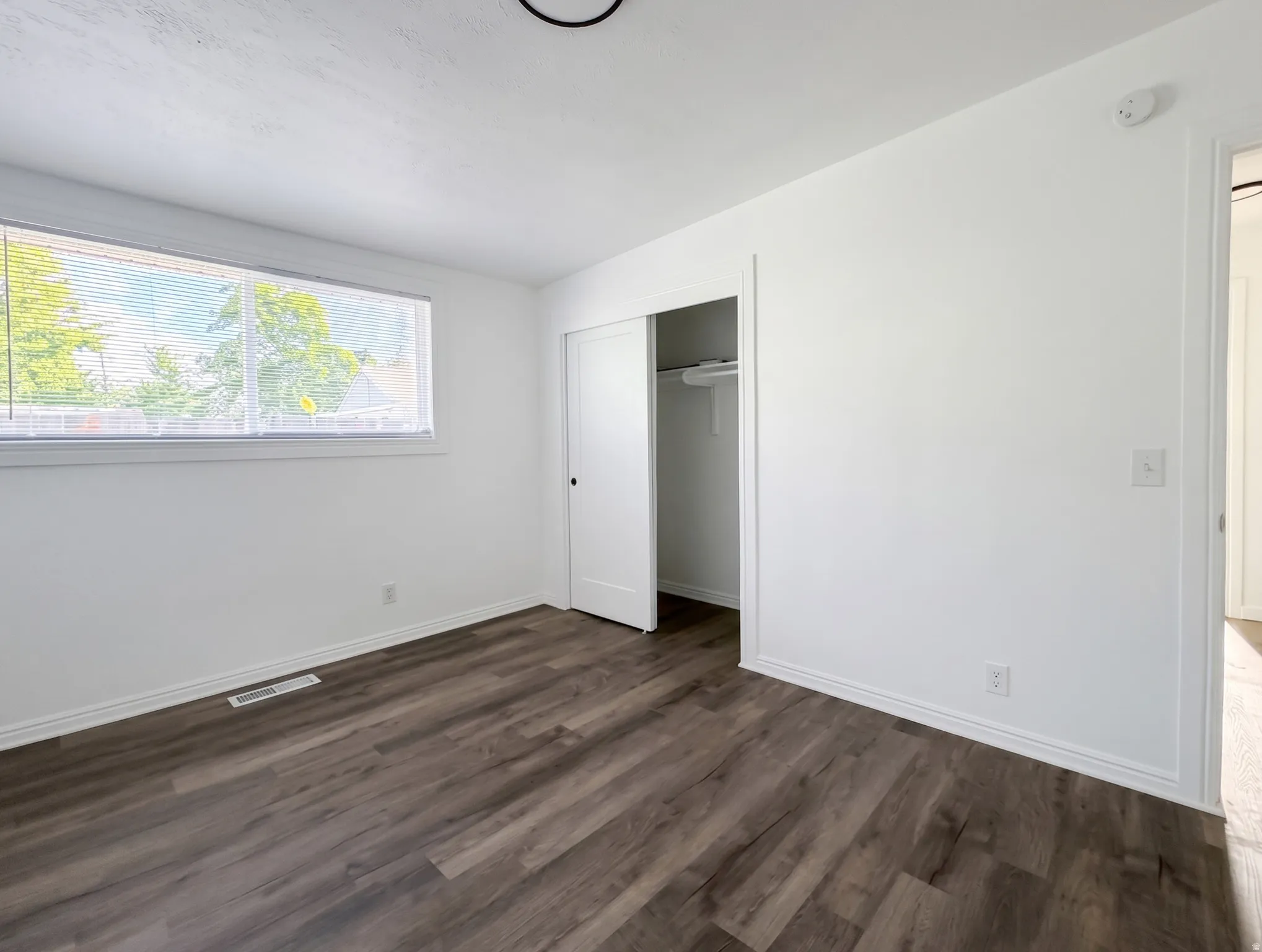 Neutral wall paint, wood-finish flooring, white trim, sliding closet door, and window