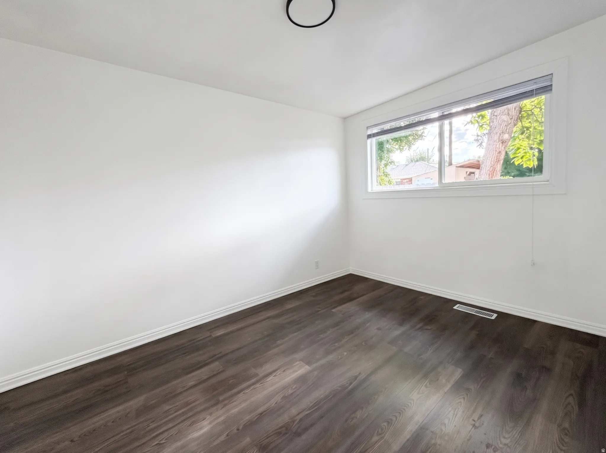 White painted walls, dark wood-finish flooring, white window trim, and a ceiling-mounted light fixture