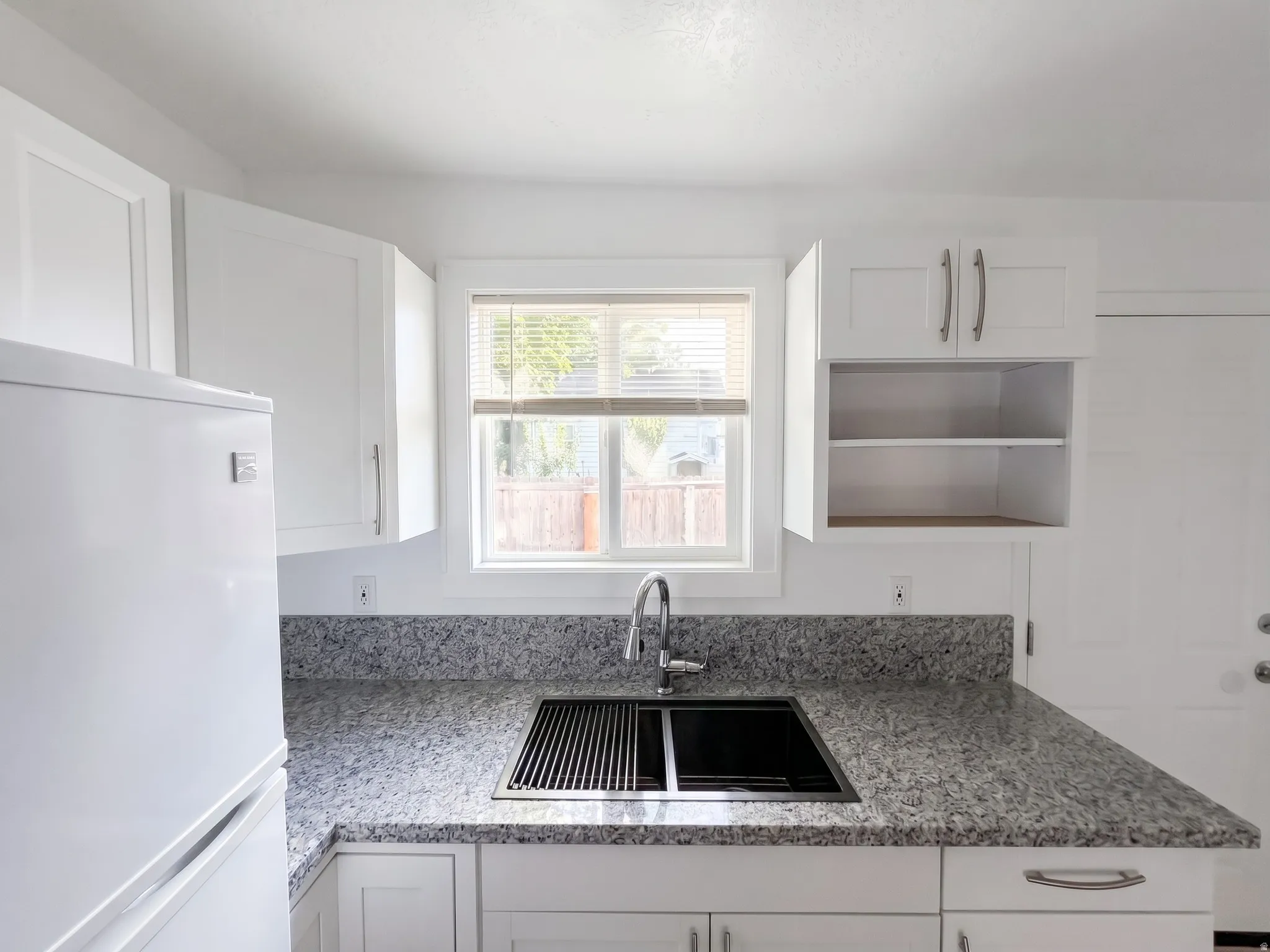 Kitchen featuring white shaker cabinetry, speckled countertops, a double-basin sink with an integrated drying rack, and a stainless steel gooseneck faucet