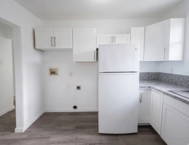 White shaker-style cabinetry, light-toned countertops, wood-finish flooring, refrigerator, laundry hook-ups.