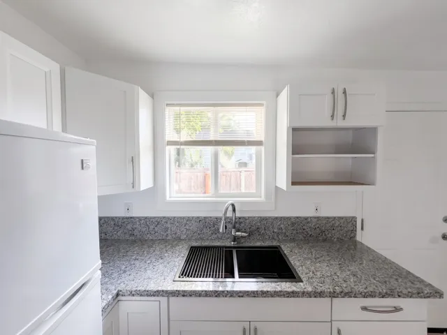 Kitchen featuring white shaker cabinetry, speckled countertops, a double-basin sink with an integrated drying rack, and a stainless steel gooseneck faucet