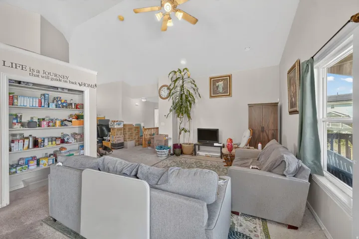 Vaulted ceiling, ceiling fan, built-in shelving, carpet flooring, and a large window with exterior view