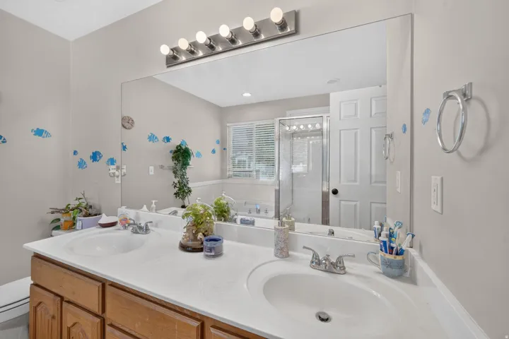 Dual vanity with integrated sinks, wood-finish cabinetry, and a full-width wall mirror with overhead bar lighting