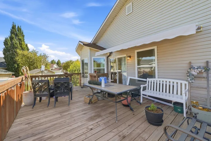 Expansive wood deck with a privacy railing, featuring a retractable awning and exterior wall-mounted lighting