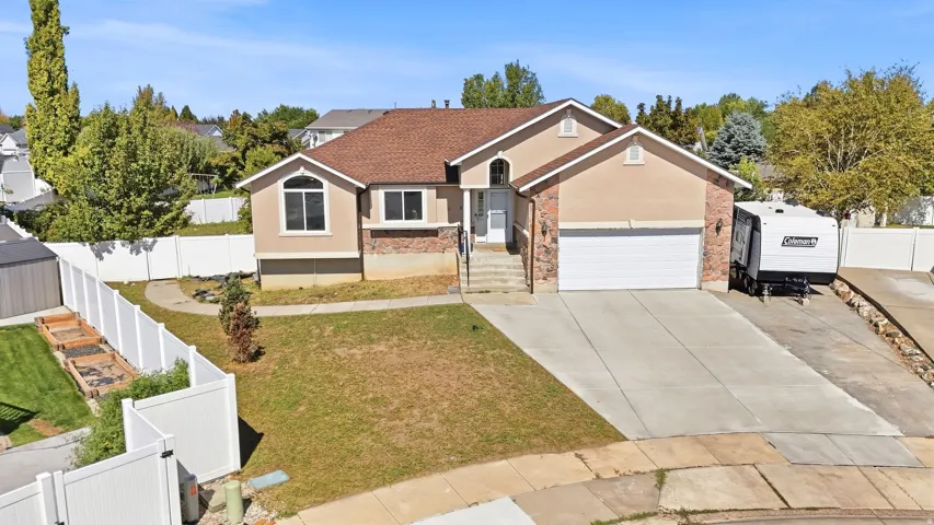 Two-story stucco and stone-faced residence featuring an attached two-car garage, concrete driveway, and white vinyl fencing