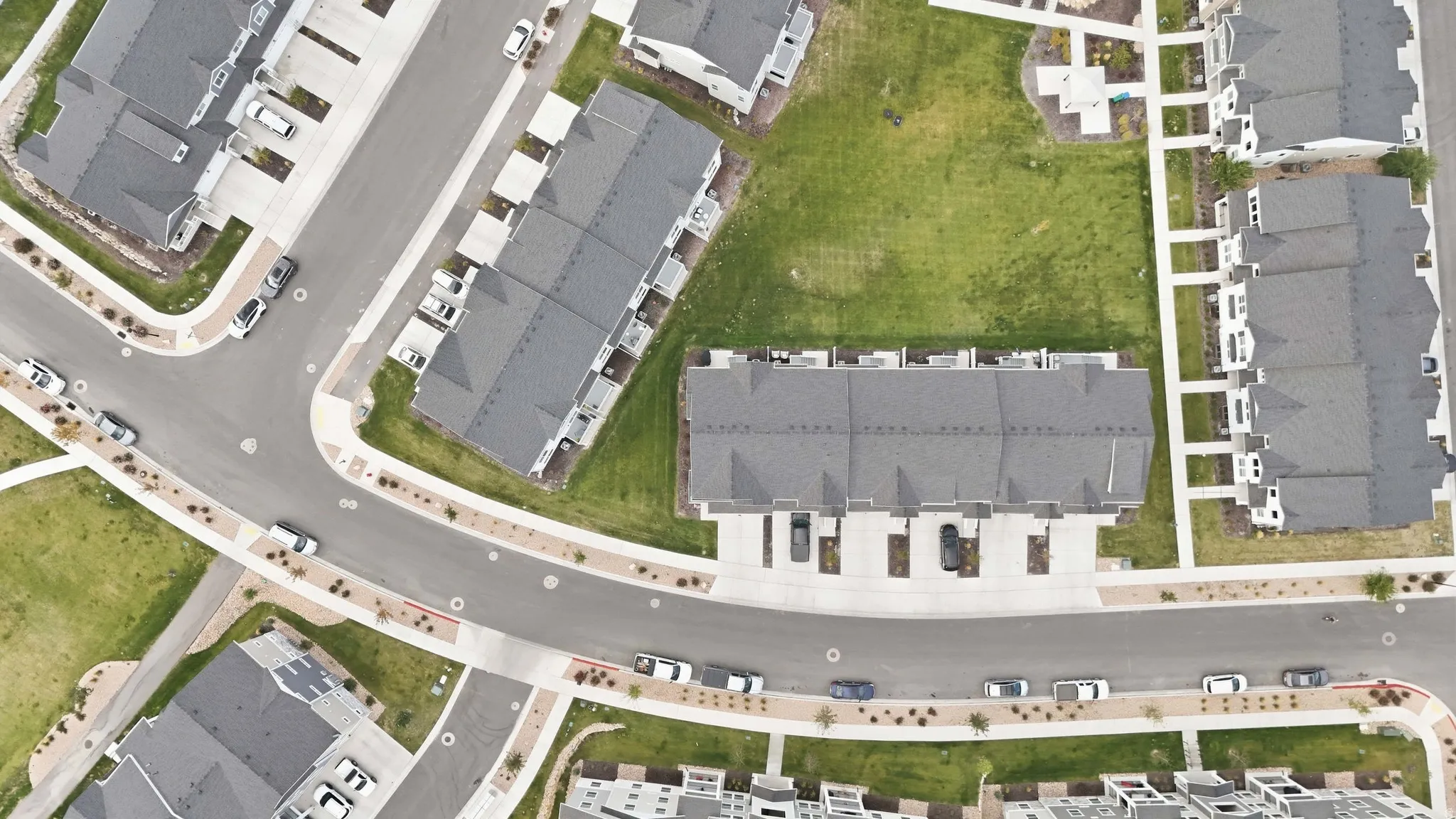 New construction townhomes with gray shingle roofing, individual paved driveways, and manicured green spaces