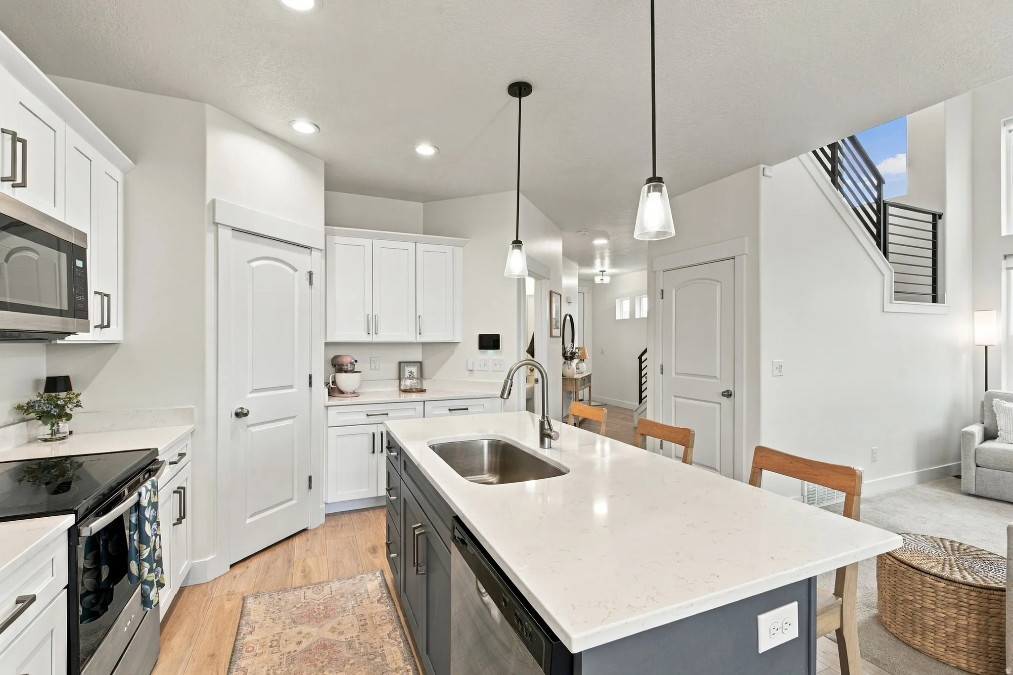 Kitchen featuring white cabinetry with dark hardware, stainless steel appliances, a center island with a sink, and white countertops