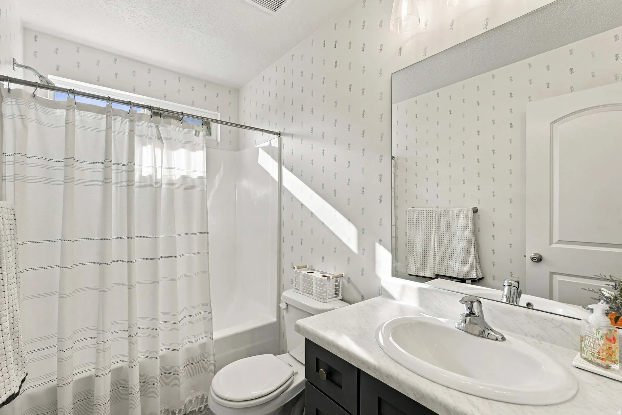 Bathroom featuring a vanity with an integrated sink, a rectangular mirror, and a shower-over-tub combination with a white surround