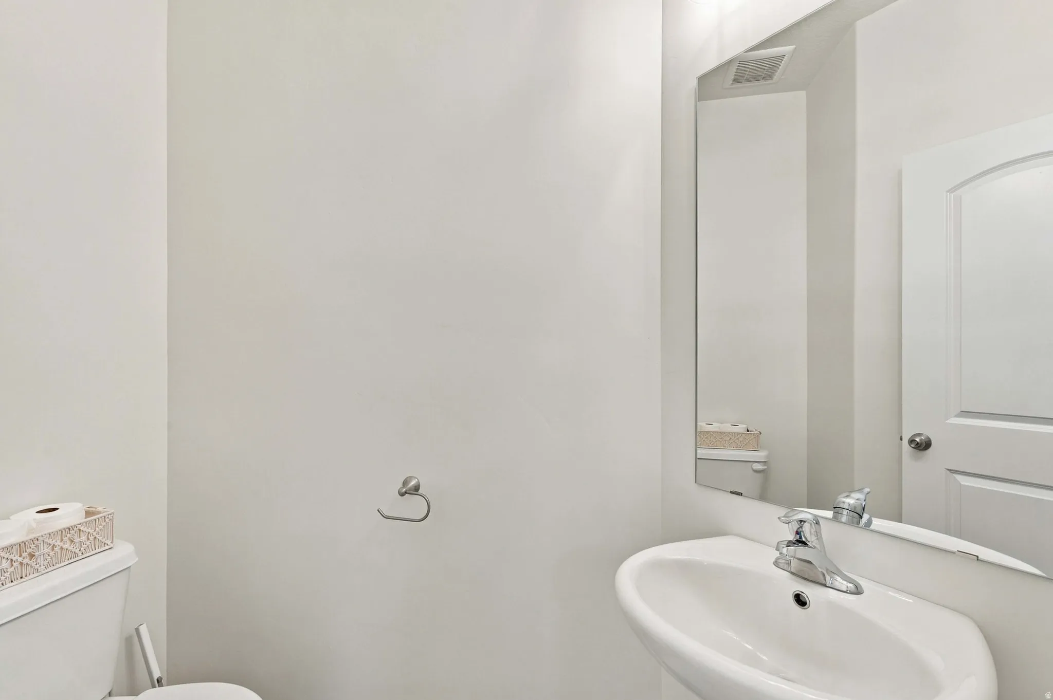 Wall-mounted basin with chrome faucet, a rectangular mirror, and an arched panel interior door