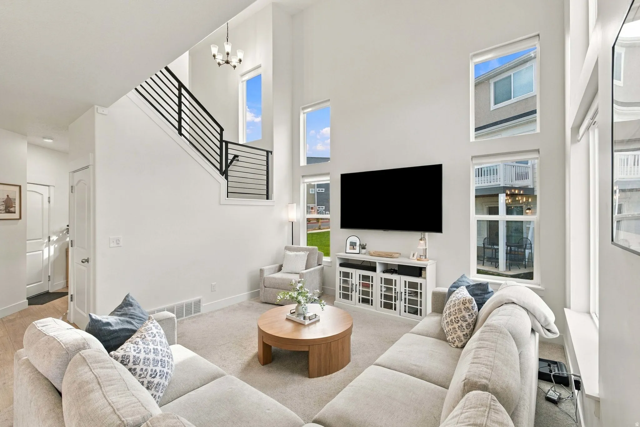 Two-story living area featuring a modern staircase with horizontal metal railings, multiple transom windows, and a built-in media console