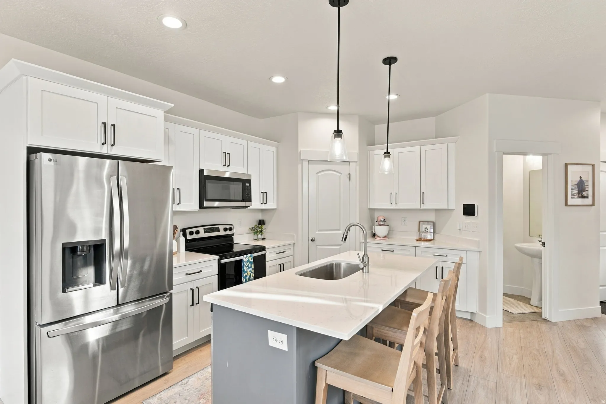 Open-concept kitchen featuring white cabinetry, stainless steel appliances, a center island with sink, pendant lighting, and wood-finish flooring