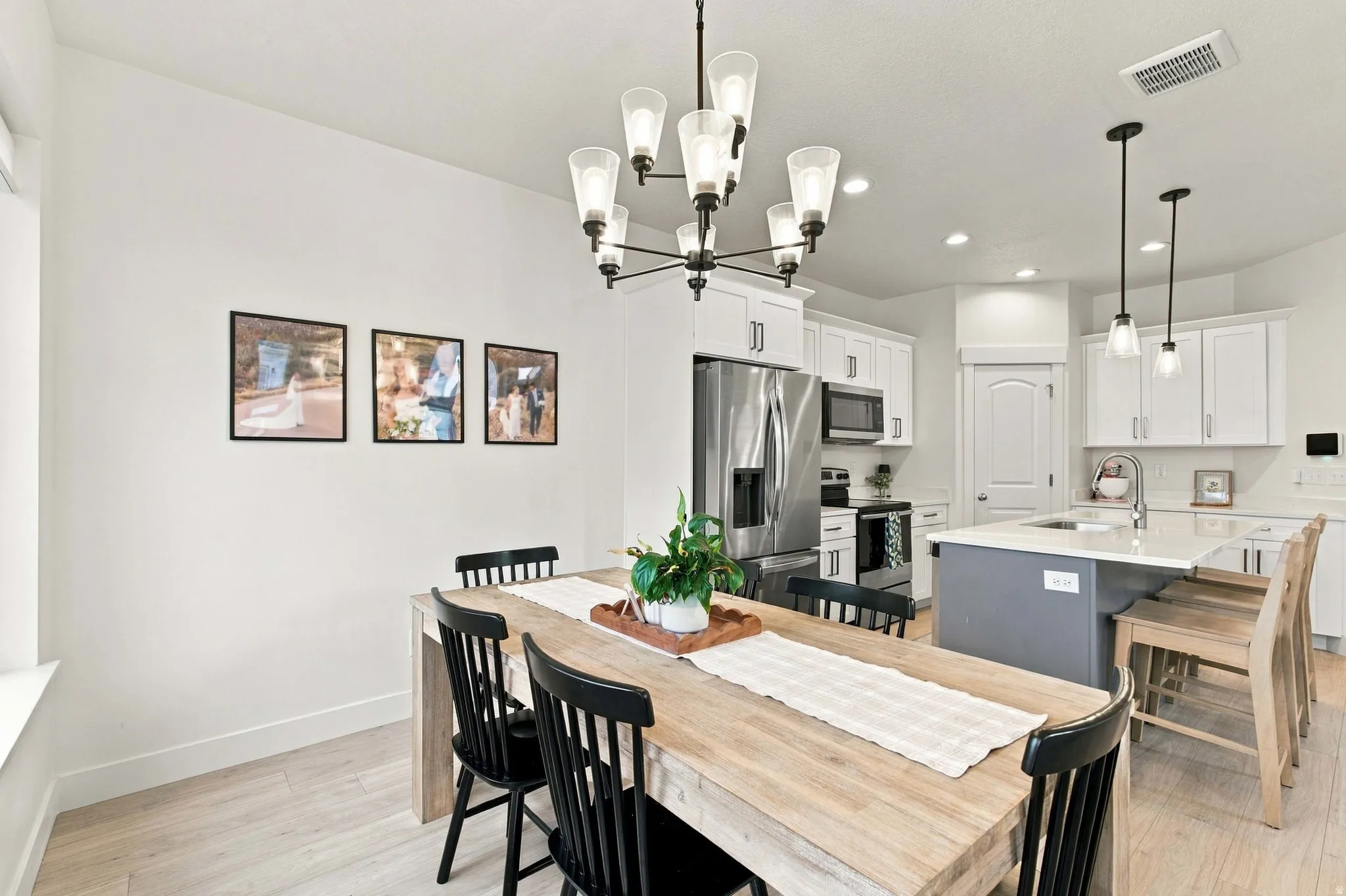 Open-concept kitchen and dining area featuring light wood-finish flooring, white cabinetry, stainless steel appliances, a center island with seating, and contemporary light fixtures