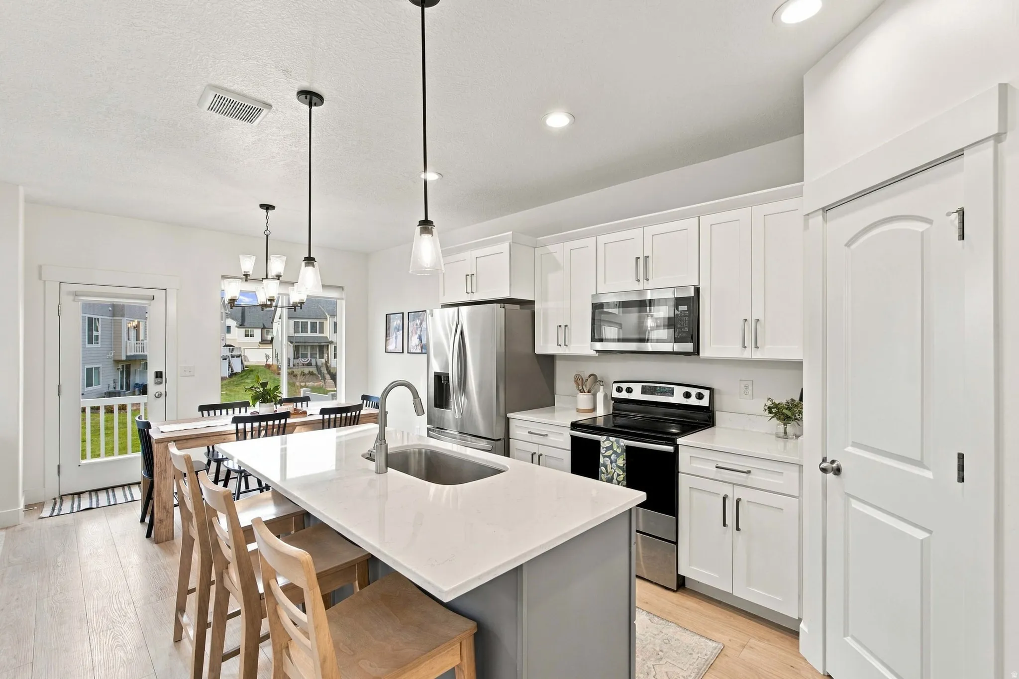 White shaker cabinetry with stainless steel appliances, a center island with a sink, pendant lighting, and wood-finish flooring