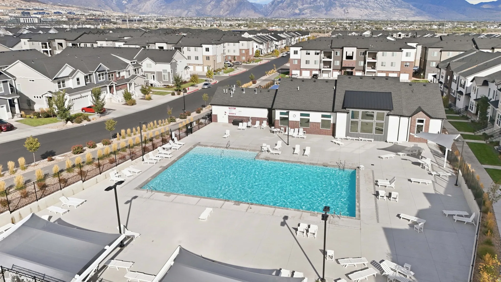 Outdoor swimming pool with integrated lighting, surrounding paved deck, and a community building with large windows