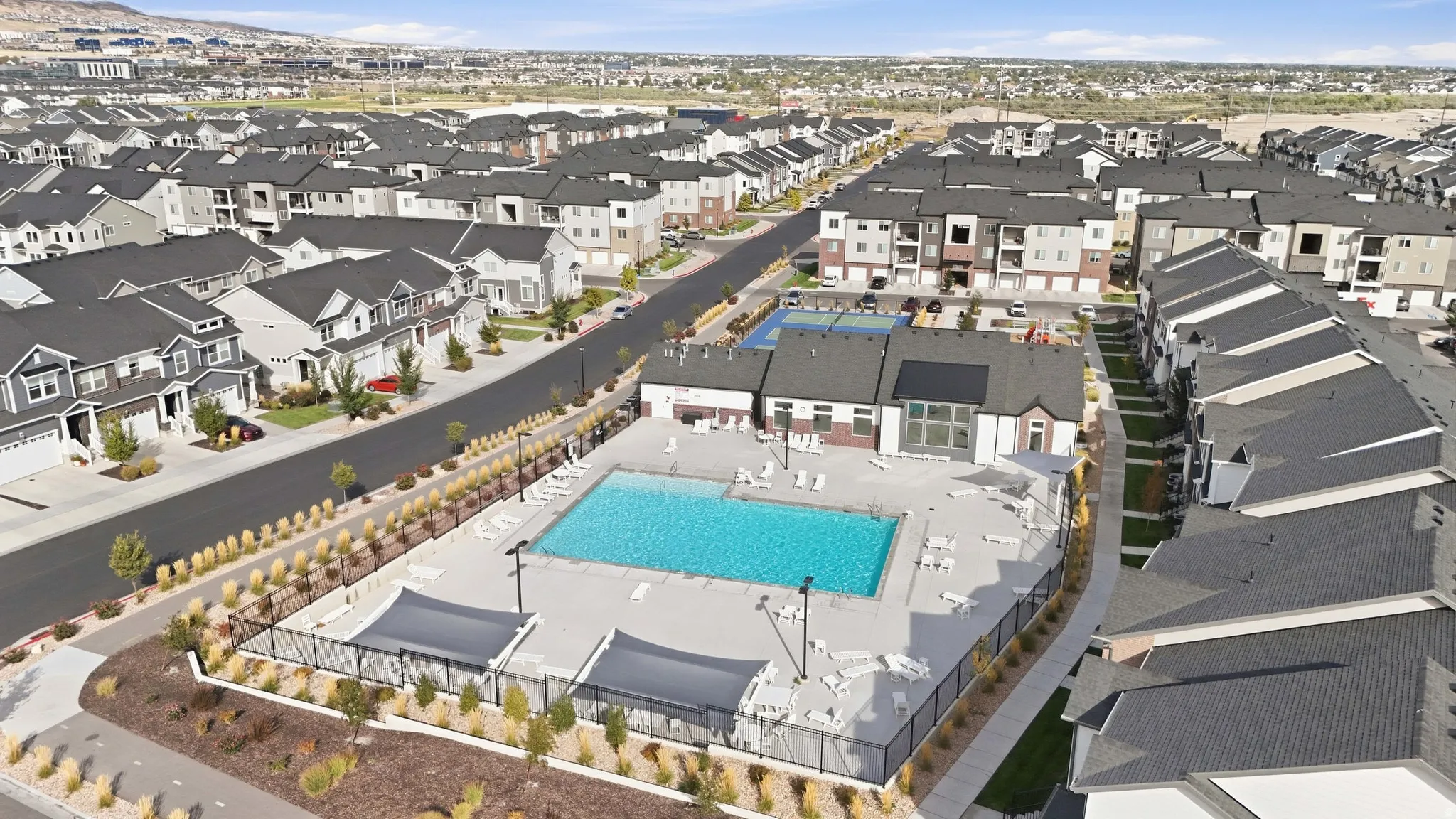 Community swimming pool with surrounding lounge chairs and shaded cabanas, hardscaped pool deck, and adjacent clubhouse building