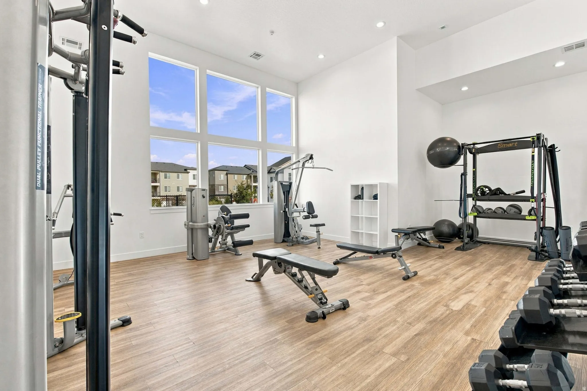 Spacious fitness area featuring expansive windows, high ceilings, wood-finish flooring, and recessed lighting