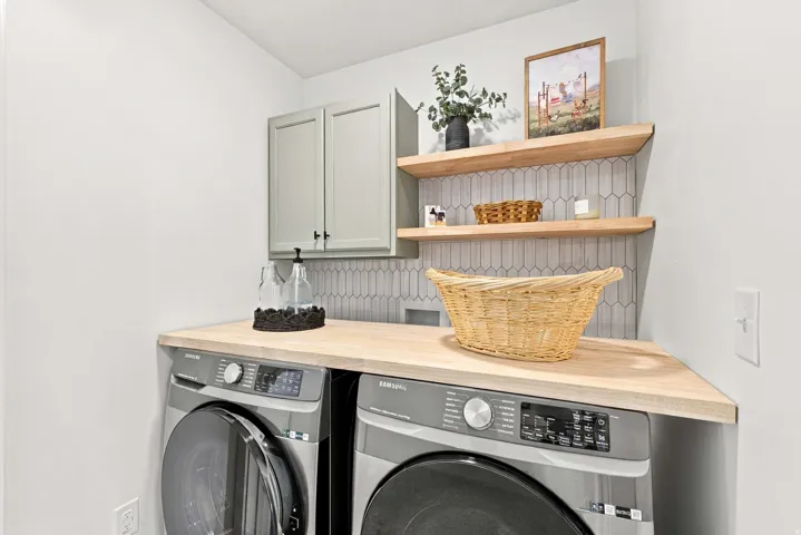 Light wood-finish countertop, floating wood-finish shelving, pale green shaker-style cabinetry, and a geometric tiled backsplash