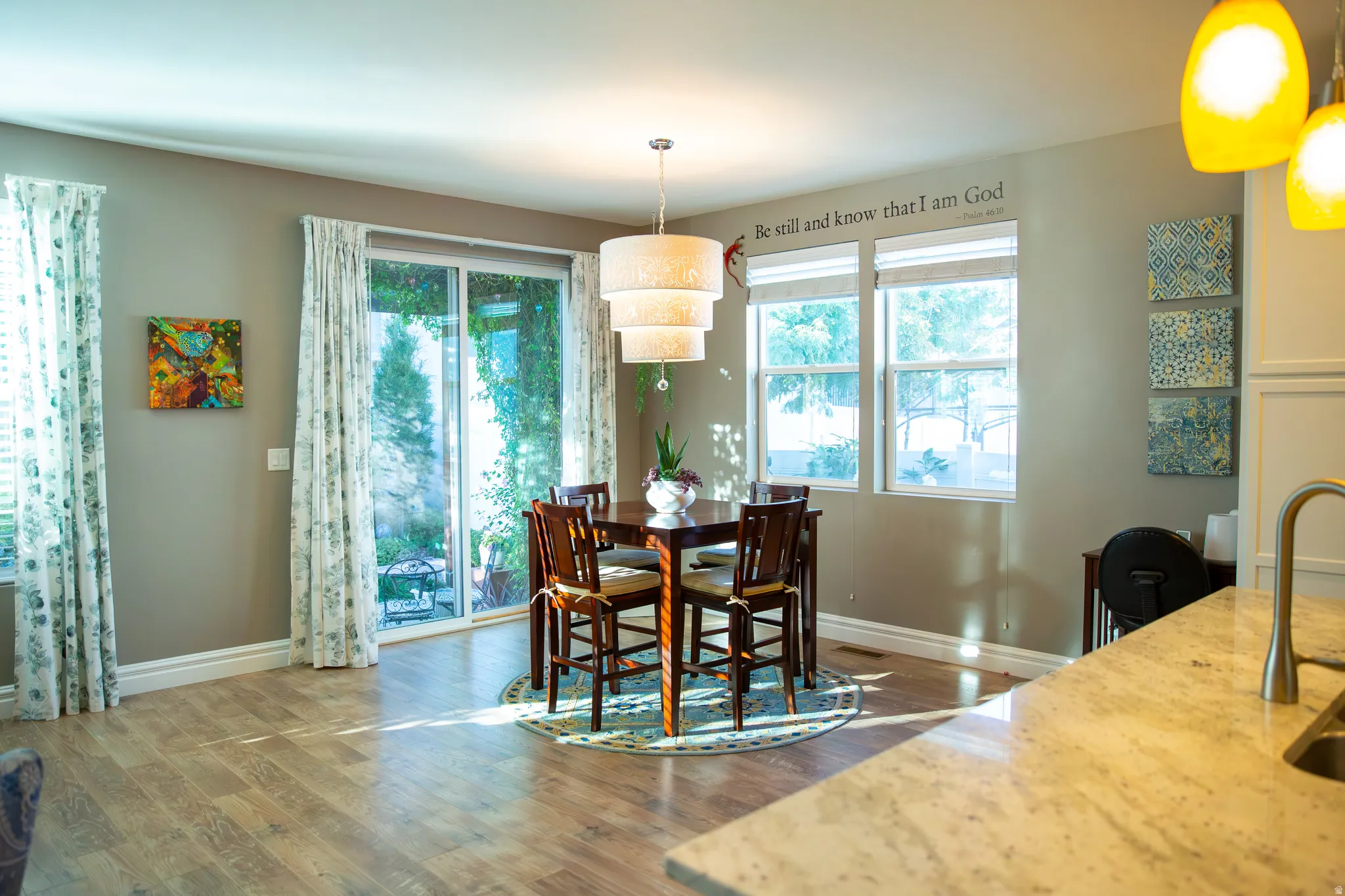 Wood-finish flooring, sliding glass door, multiple windows, layered drum pendant light, and a stone-finish countertop