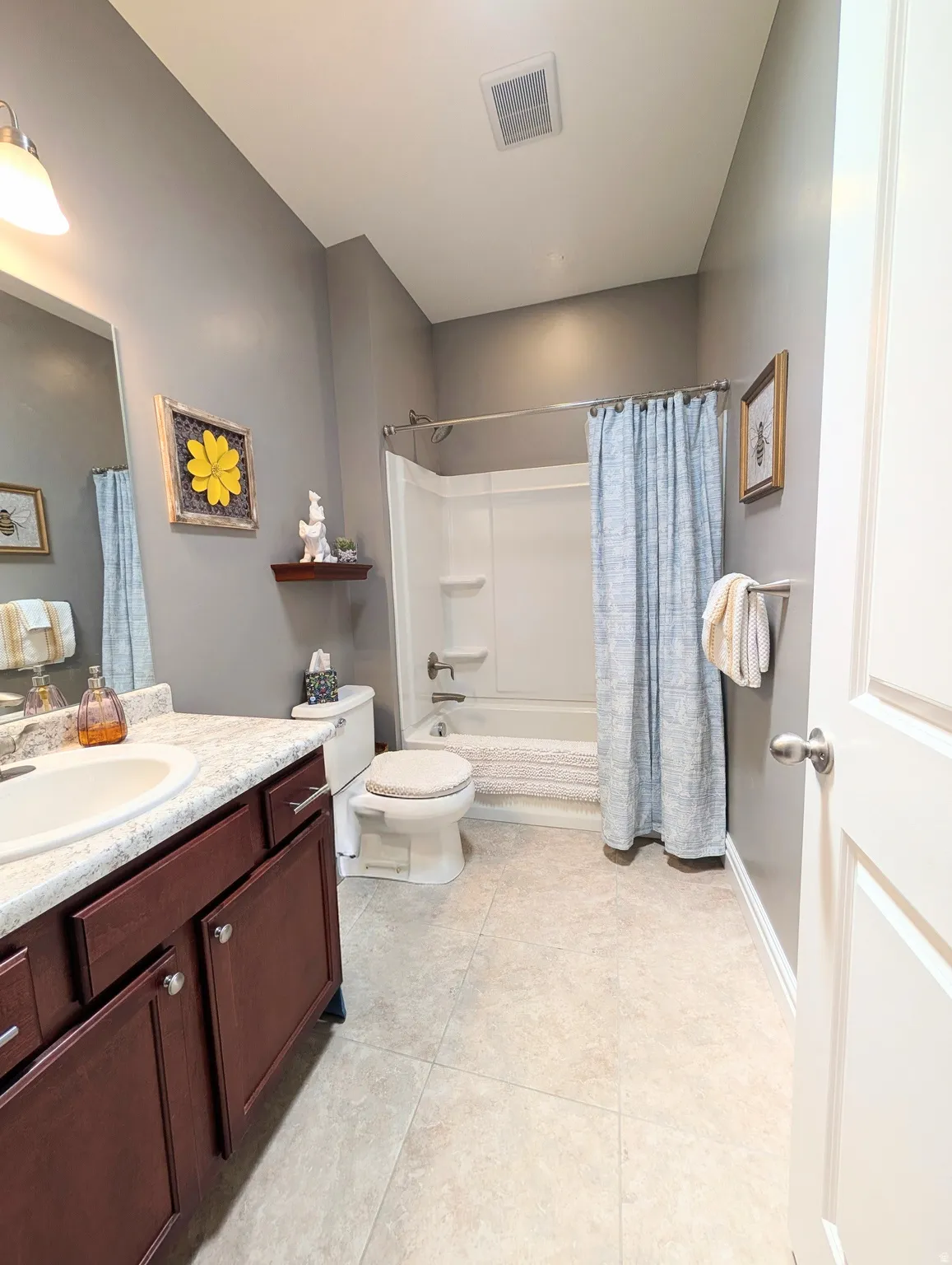 Warm-toned tile flooring, rich wood-finish vanity with an integrated sink, and a combination tub and shower