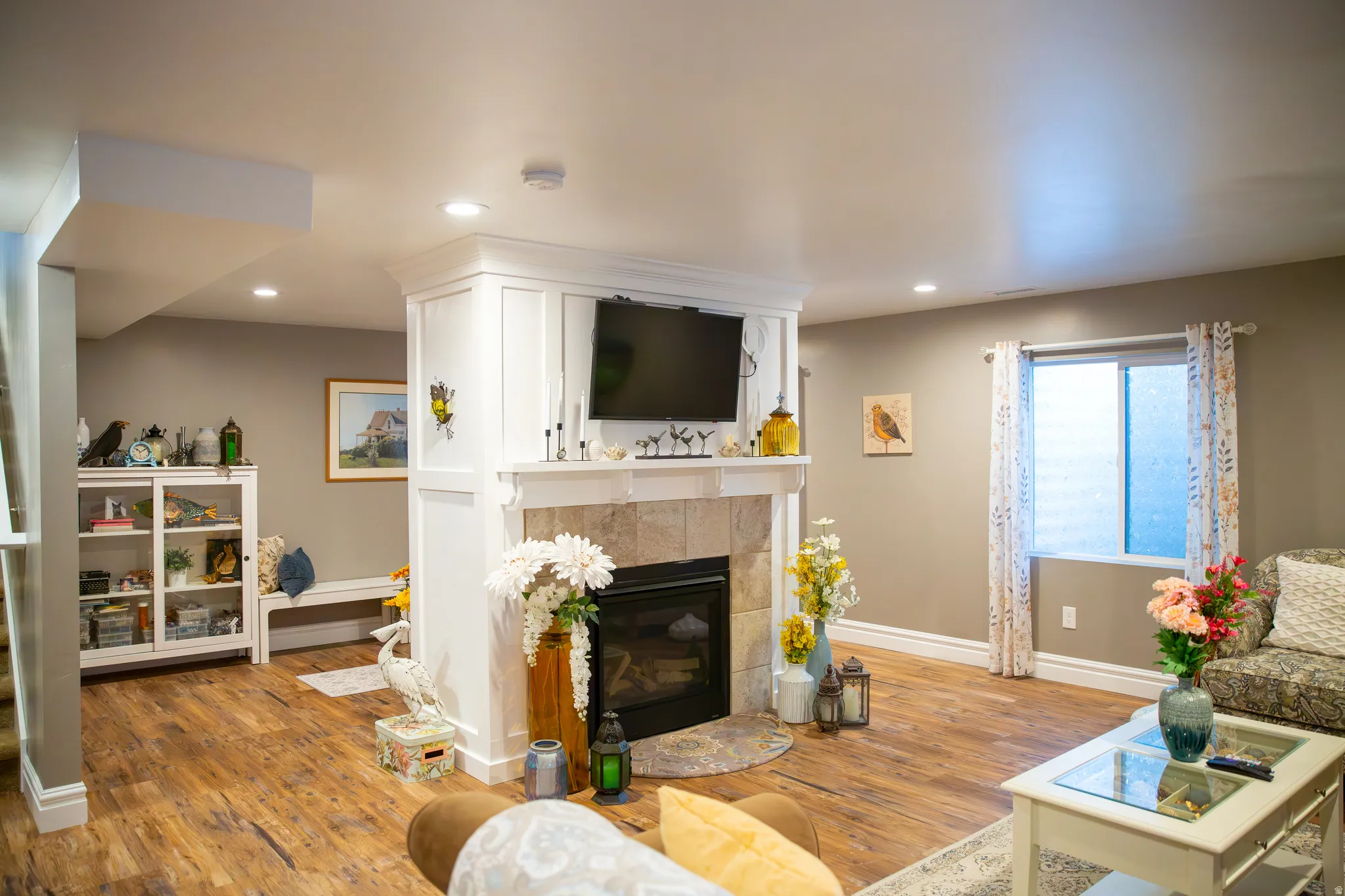 Built-in fireplace with a stone surround and white wood mantel, recessed lighting, wood-finish flooring, and a built-in display cabinet with glass doors