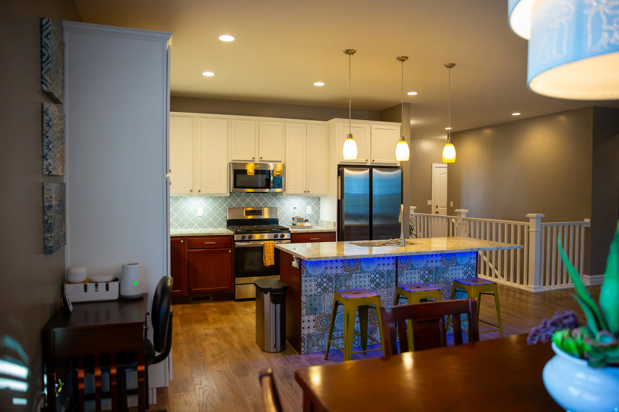 Kitchen featuring stainless steel appliances, a tile backsplash, wood-finish flooring, and a kitchen island with pendant lighting