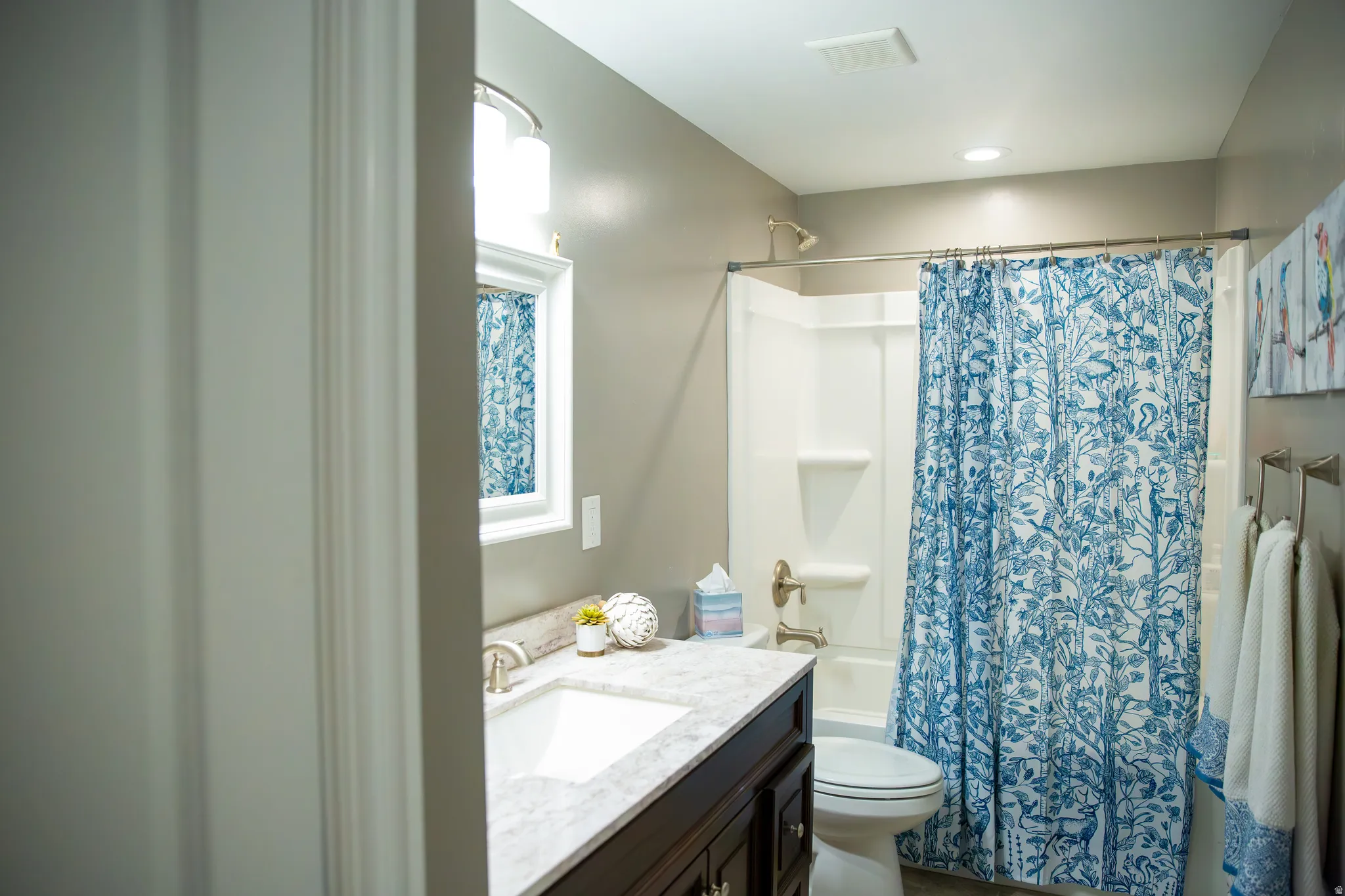 Bathroom featuring a vanity with an integrated sink, a built-in bathtub with shower, a window with trim, and a toilet