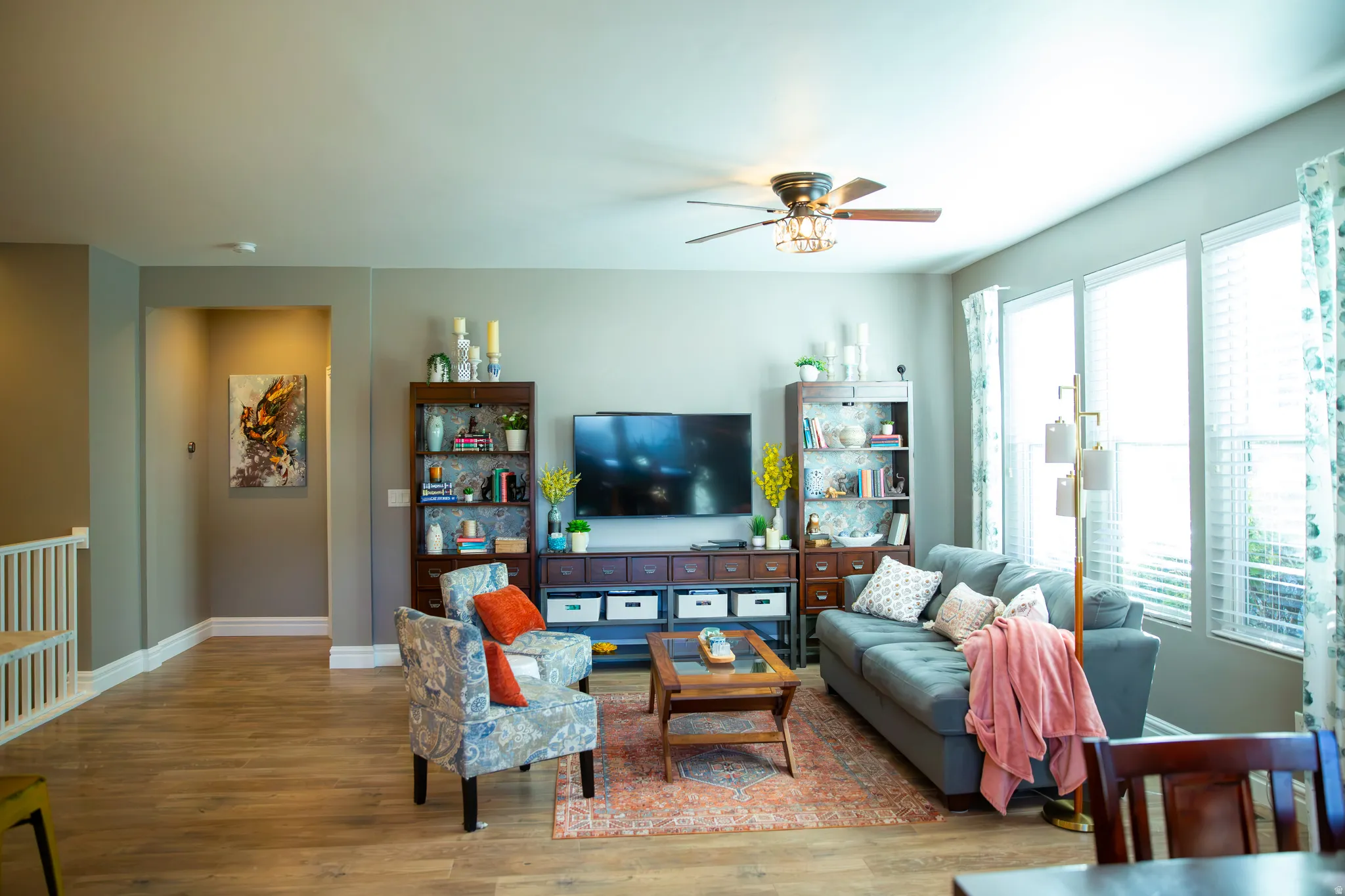 Wood-finish flooring throughout, ceiling fan with integrated lighting, multiple windows with blinds, and neutral wall tones