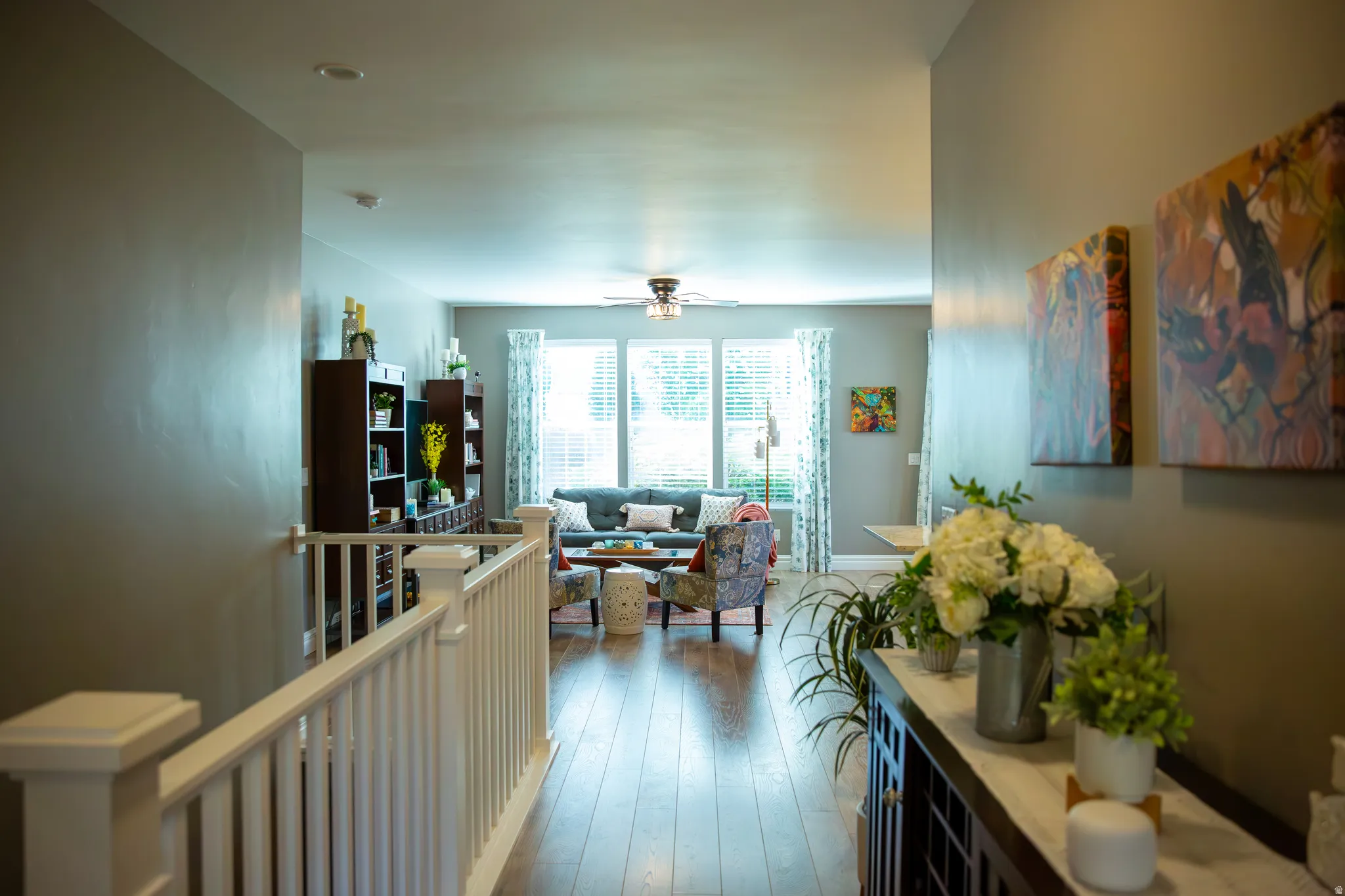 Wood-finish flooring throughout, white painted railing, recessed lighting, and living area with multiple windows