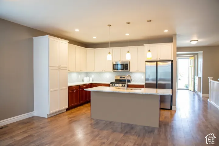 Spacious kitchen featuring white upper cabinetry, rich wood-finish lower cabinetry, stainless steel appliances, and an expansive island with a sink and pendant lighting