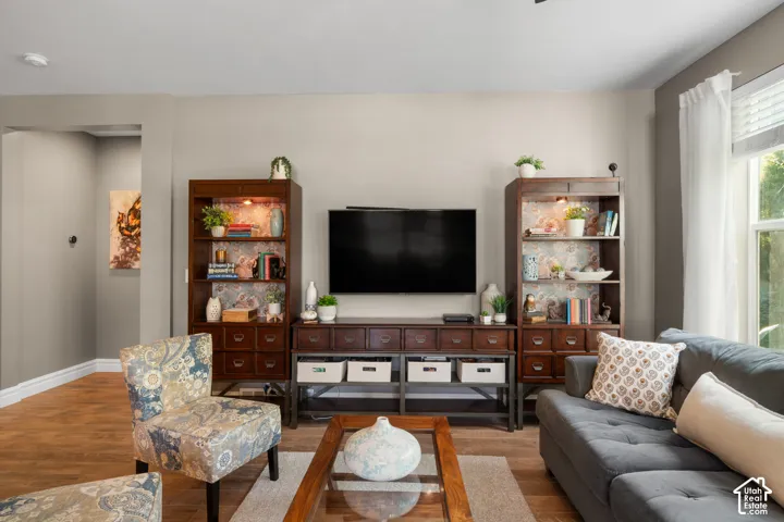 Wood-finish flooring throughout, light-toned wall paint, and a white-trimmed window with sheer drapes