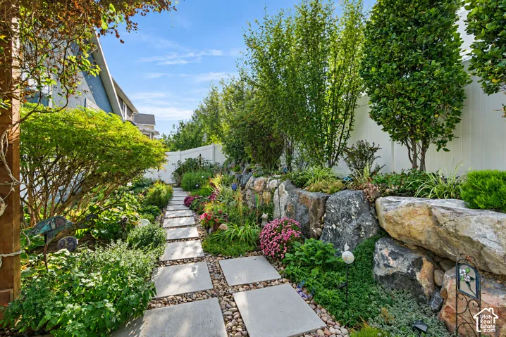 Stone pathway with square pavers and river rock, flanked by lush landscaping and a natural rock retaining wall