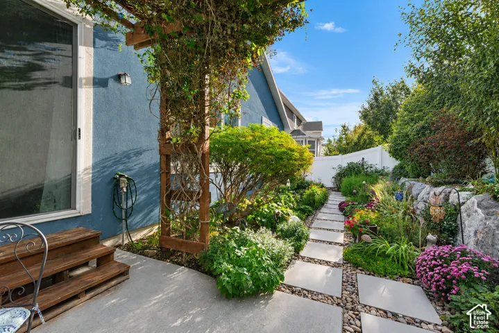 Stucco exterior with a sliding glass door, leading to a concrete patio with wooden steps and a wooden pergola