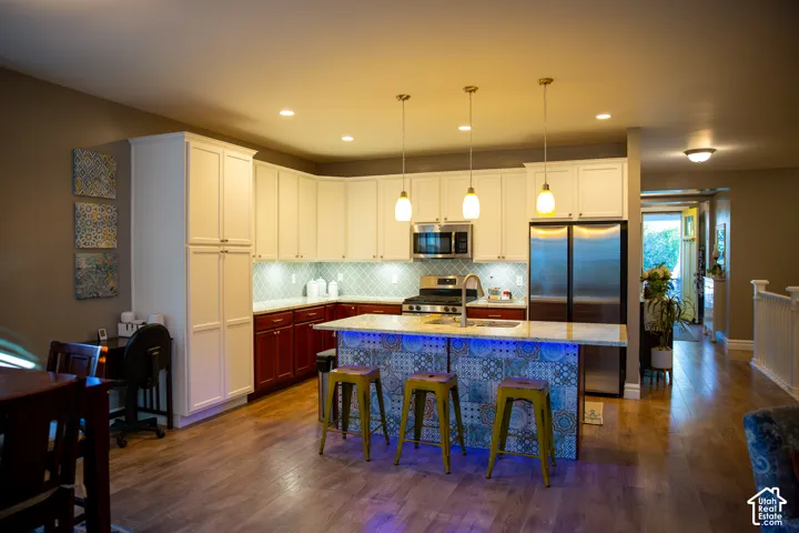 Kitchen featuring wood-finish flooring, two-tone cabinetry, stainless steel appliances, and a tiled backsplash