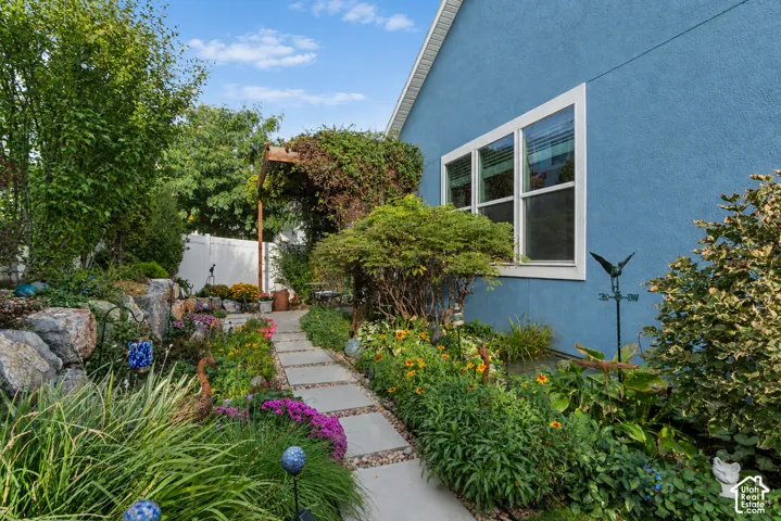 Landscaped side yard featuring a concrete paver pathway, mature plantings, a rock garden, and a wood trellis