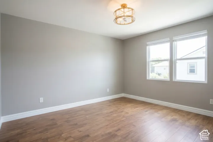 Neutral gray wall paint, wood-finish flooring, white trim, two white-framed windows, and a gold-finish drum ceiling fixture