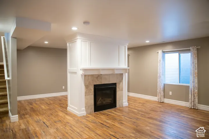 Recessed lighting, wood-finish flooring, and a built-in fireplace with a stone surround and white mantel