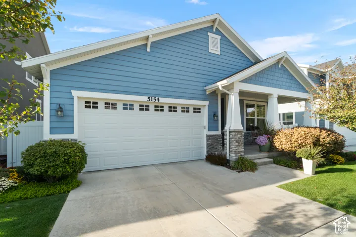 Exterior featuring blue siding, white trim, a covered entry with stone accents, a concrete driveway, and established landscaping