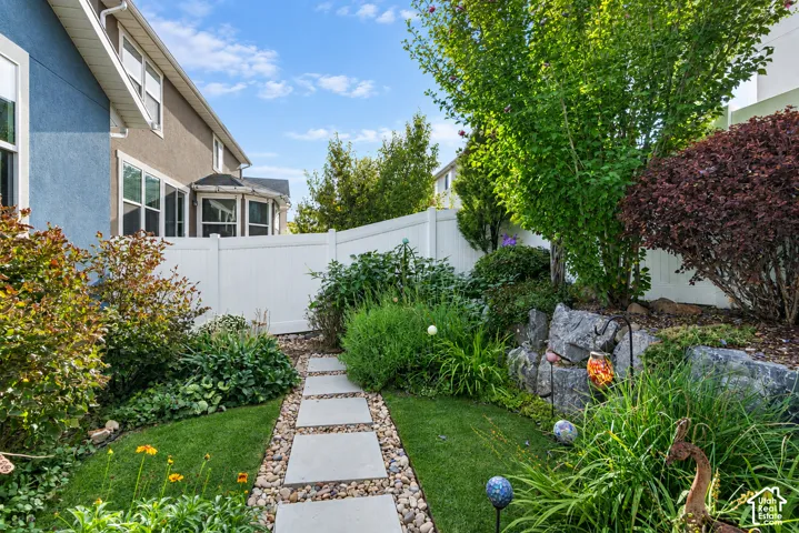 Manicured backyard with a stone-edged garden bed, lush plantings, a concrete paver pathway, and a privacy fence