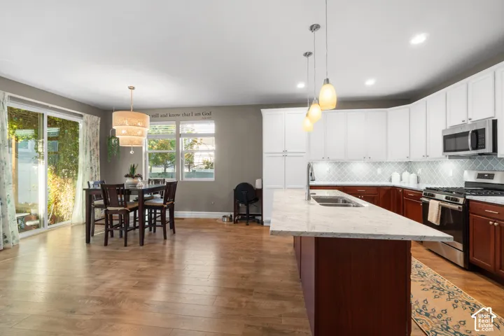 Open-concept kitchen and dining area featuring wood-finish flooring, a kitchen island with dual sinks, white upper cabinetry, and stainless steel appliances