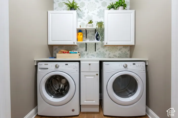Laundry area featuring wood-finish flooring, white cabinetry, integrated countertop, and a decorative wallpaper accent