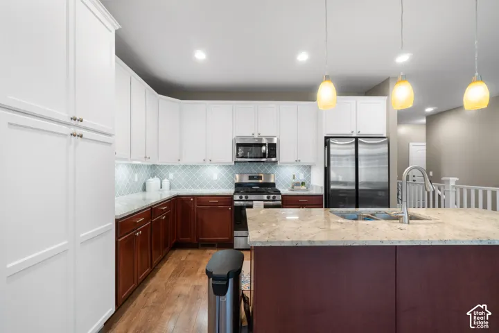 Gourmet kitchen featuring white upper cabinetry, rich wood-finish lower cabinetry, stainless steel appliances, a tile backsplash, and a large central island with a sink