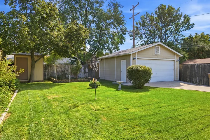 Detached garage with a white overhead door and side entry, featuring exterior lighting